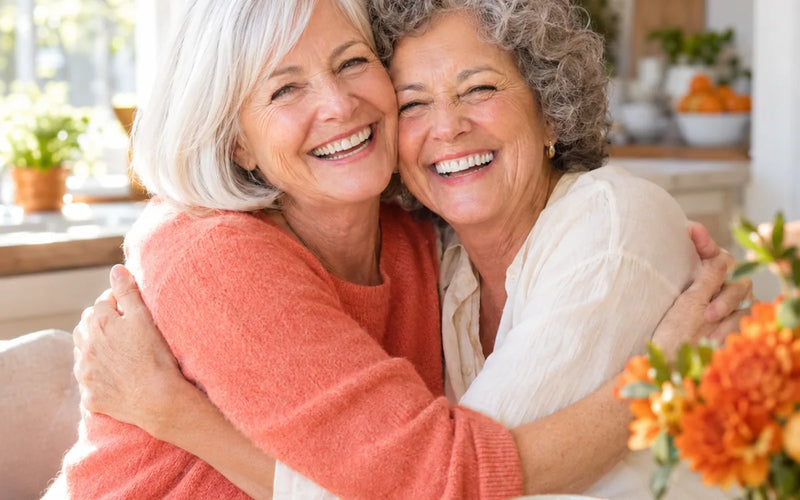 Two women in their sixties laughing in a close hug in a kitchen