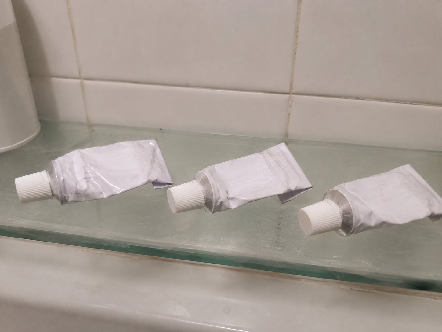 Three half-used tubes of antifungal cream on a bathroom shelf