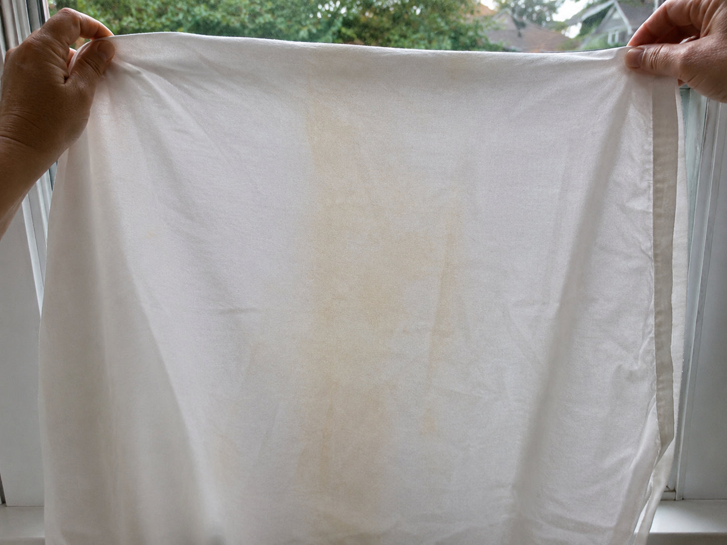 A white pillowcase held up to the light showing faint yellowish marks