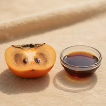 A halved persimmon next to a dish of persimmon tannin